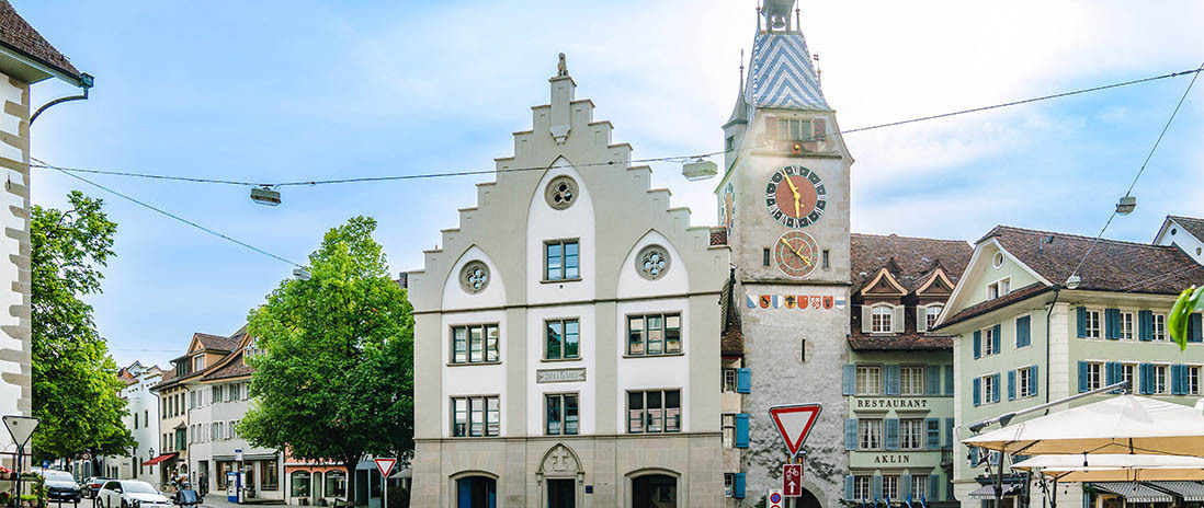Der Zytturm am Kolinplatz in Zug, flankiert von historischen Gebäuden und Gastronomie in der Nähe des Neubauprojekts Colin.