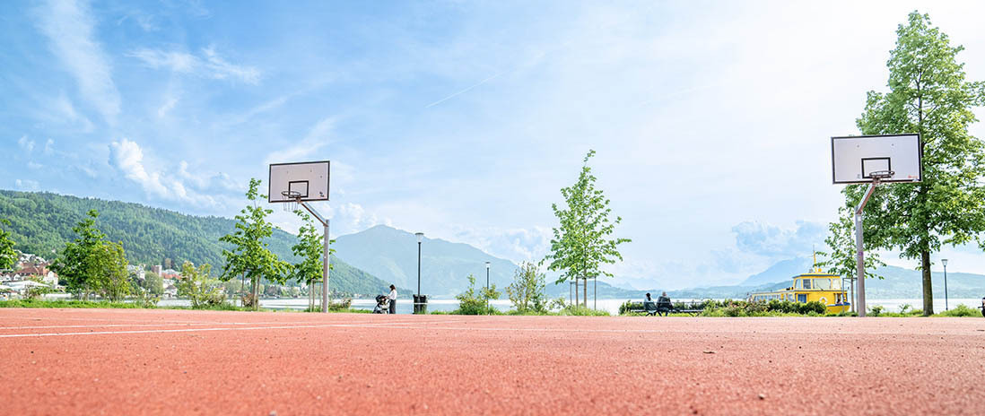 Offener Basketballplatz an der Zuger Seepromenade mit Blick auf den See und die umliegenden Berge – Freizeitangebot im Grünen in der Nähe des Neubauprojekts Colin.