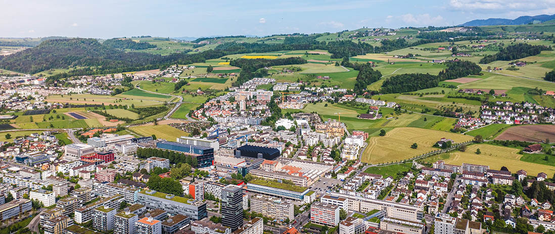 Grossflächige Ansicht der Region Zug mit Wohnsiedlungen, Grünflächen und angrenzenden Hügeln in der Nähe des Neubauprojekts Colin.