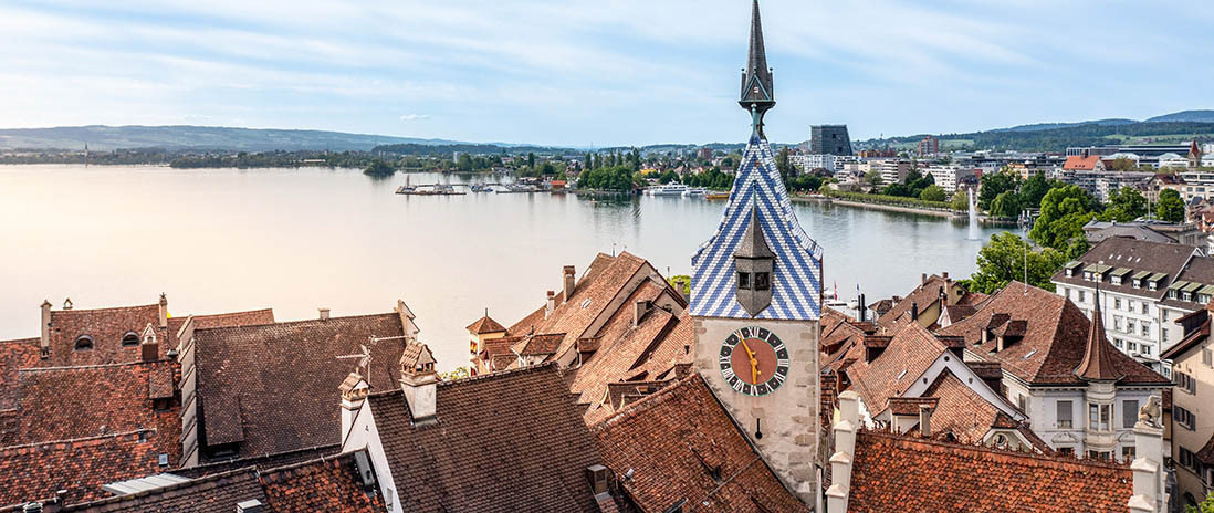 Zuger Zytturm mit Uhrendach in der Altstadt Zug in Draufsicht, im Hintergrund der Zugersee und die Seepromenade in der Nähe des Neubauprojekts Colin..